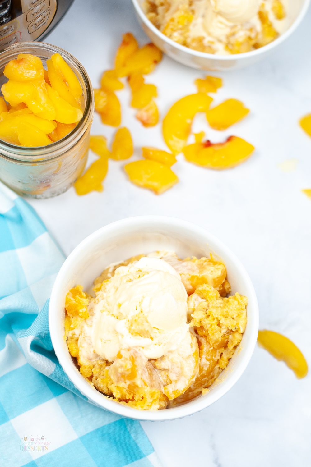 Image of instant pot peach cobbler in a white bowl, topped with vanilla ice cream
