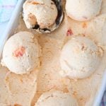 A few balls of peach ice cream in an ice cream container
