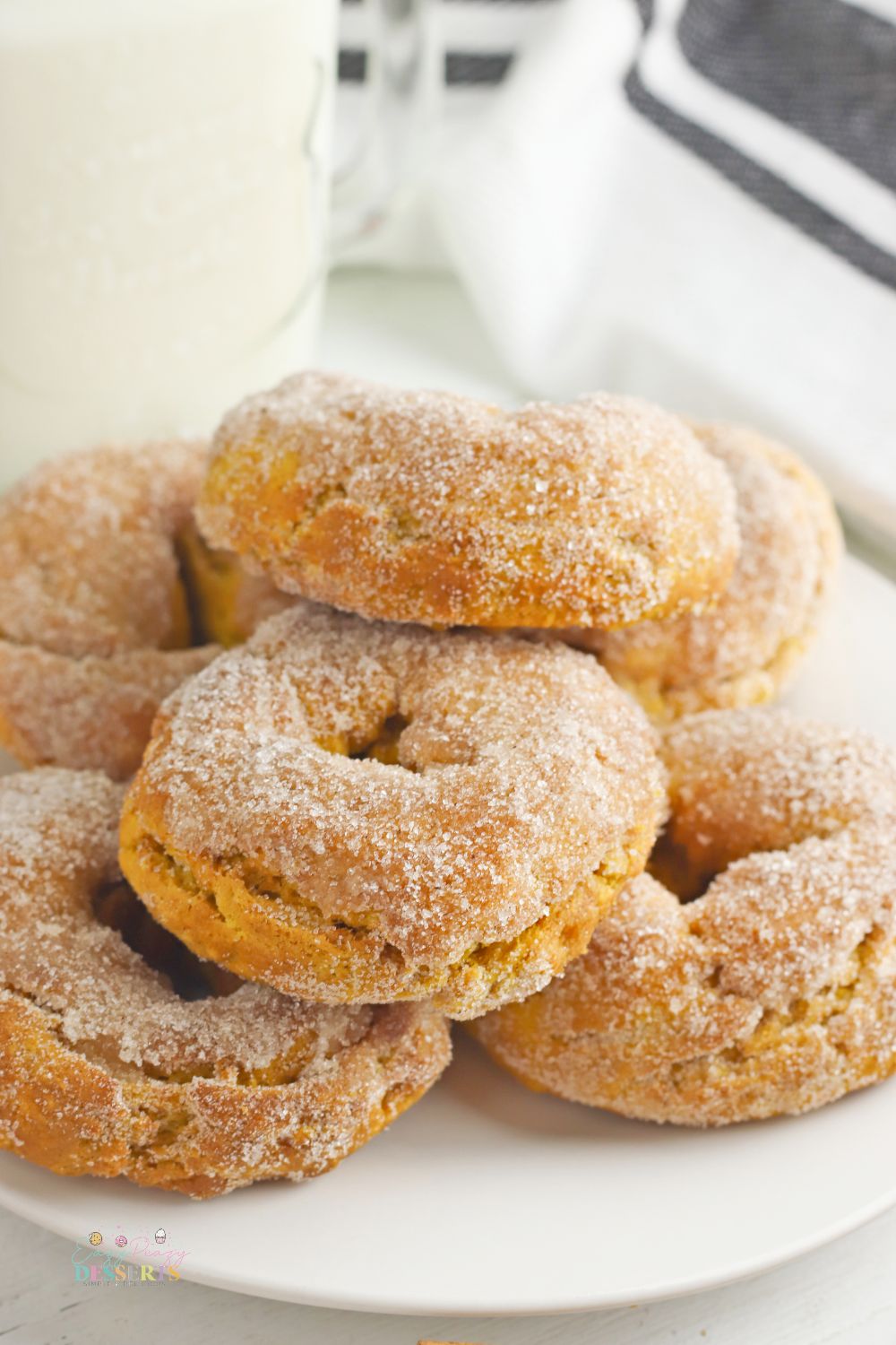 Air fryer pumpkin donuts on a white serving plate next to a glass of milk