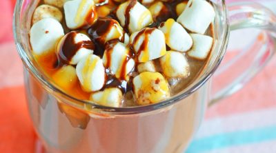 Boozy hot chocolate in a mug, decorated with marshmallows and chocolate caramel syrup