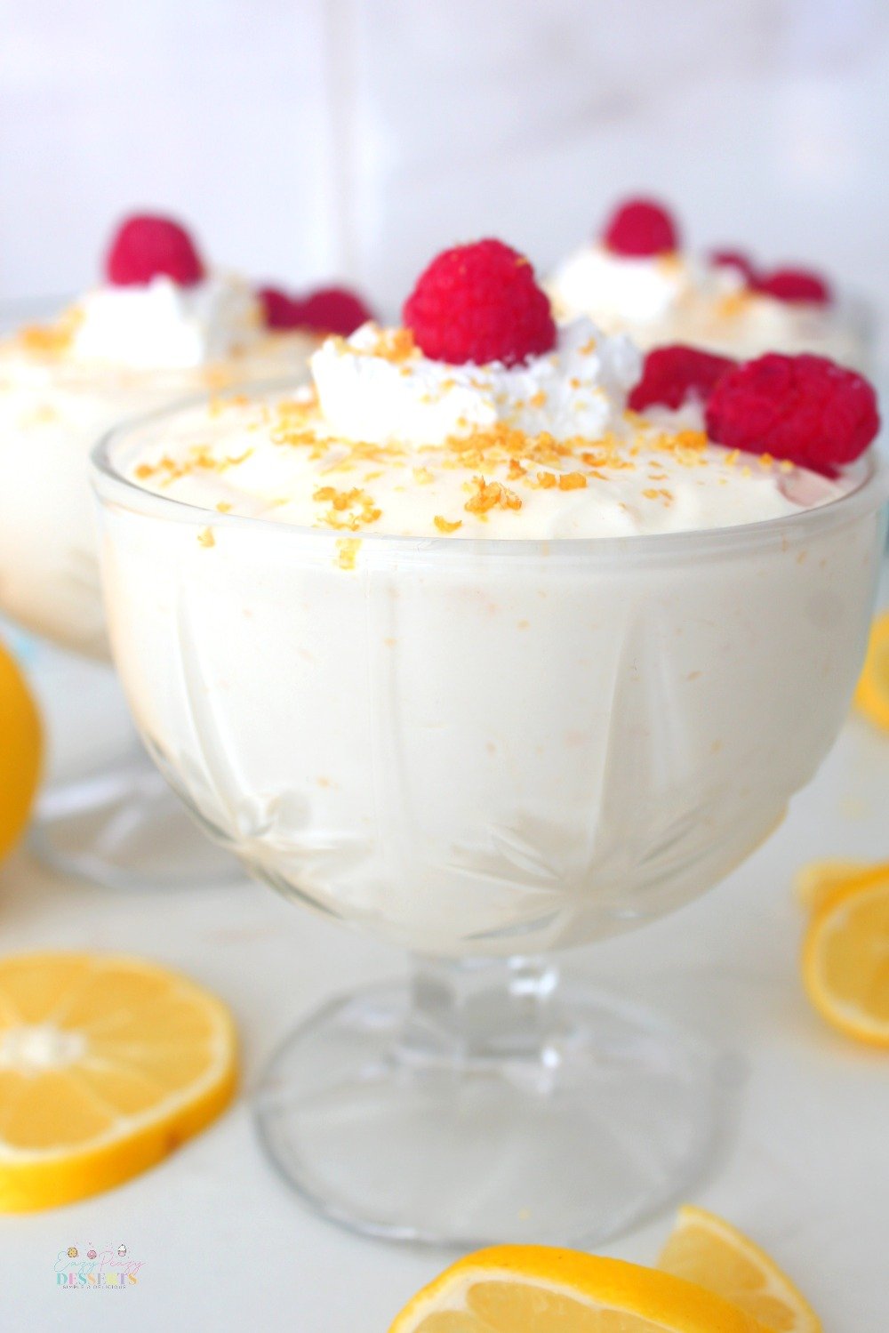 Close up image of lemon cheesecake mousse served in an ice cream cup and decorated with raspberries, lemon zest and whipped cream