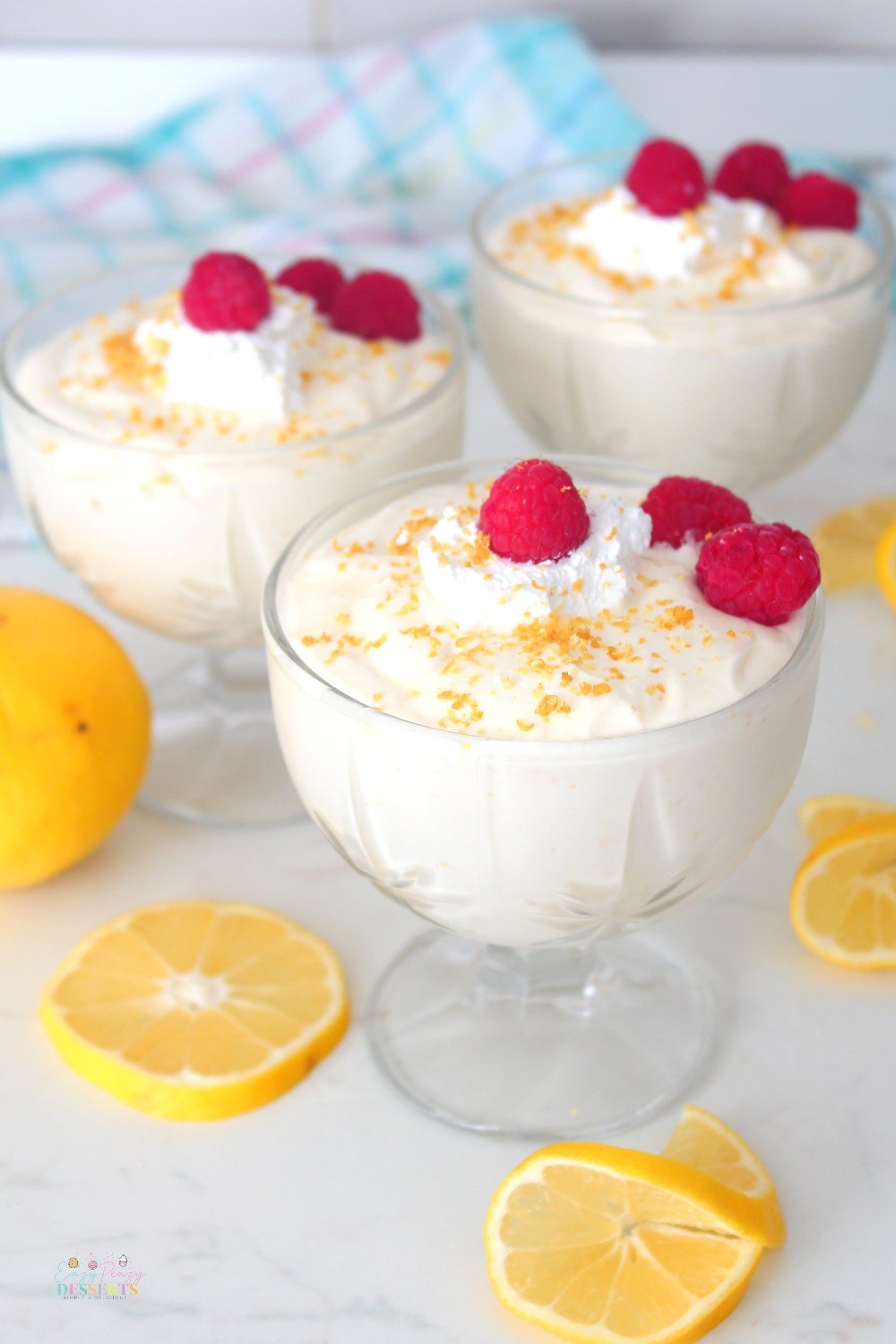 Image of three ice cream cups, filled with lemon mousse, decorated with raspberries, whipped cream, lemon zest and lemon slices