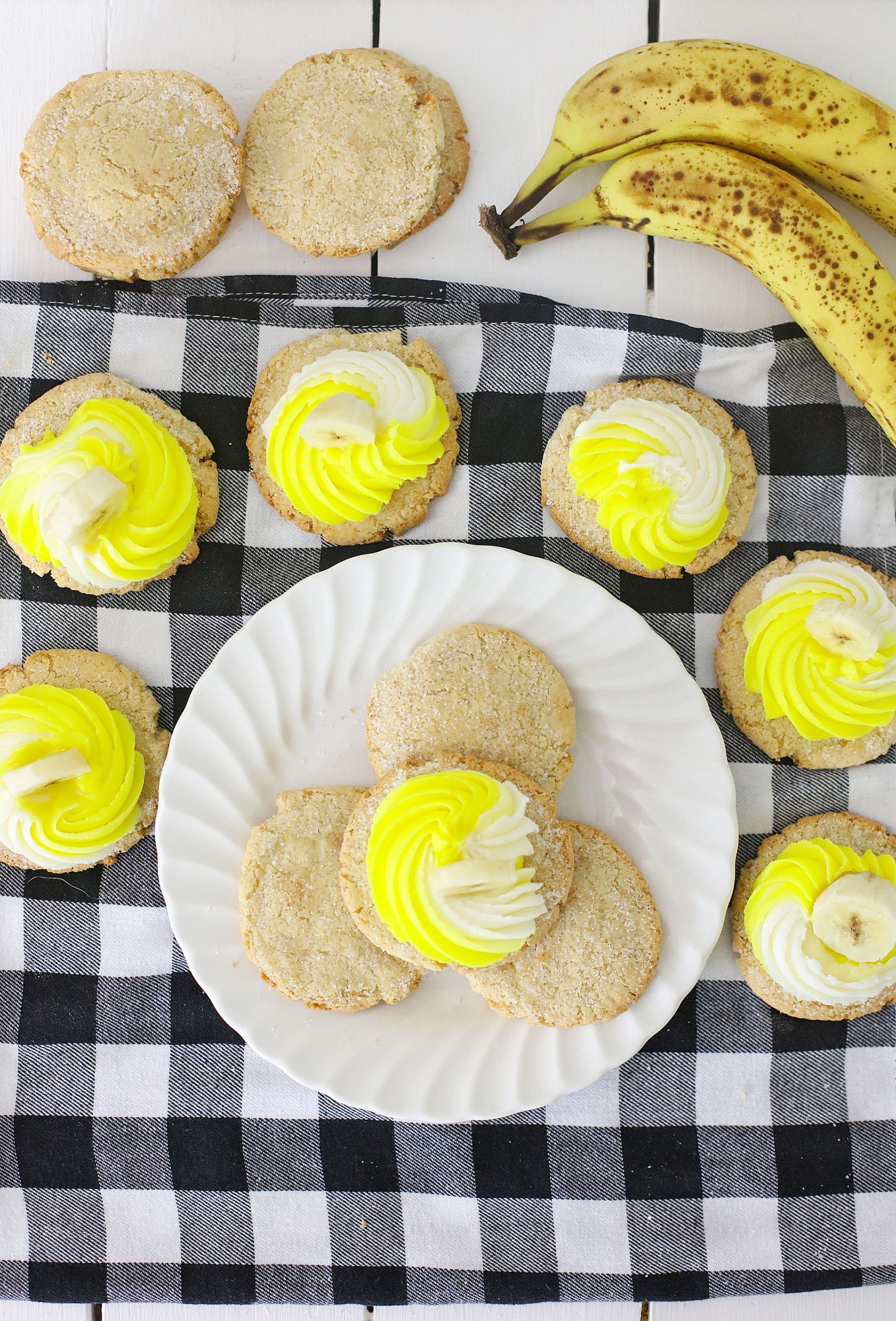 Overhead image of banana cookies decorated with white and yellow cream cheese frosting and banana slices