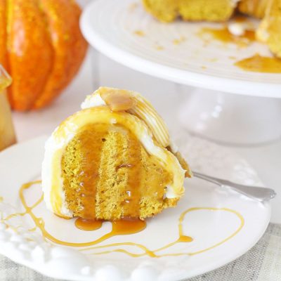 Close up image of a slice of pumpkin bundt cake with buttercream frosting, drizzled with caramel sauce