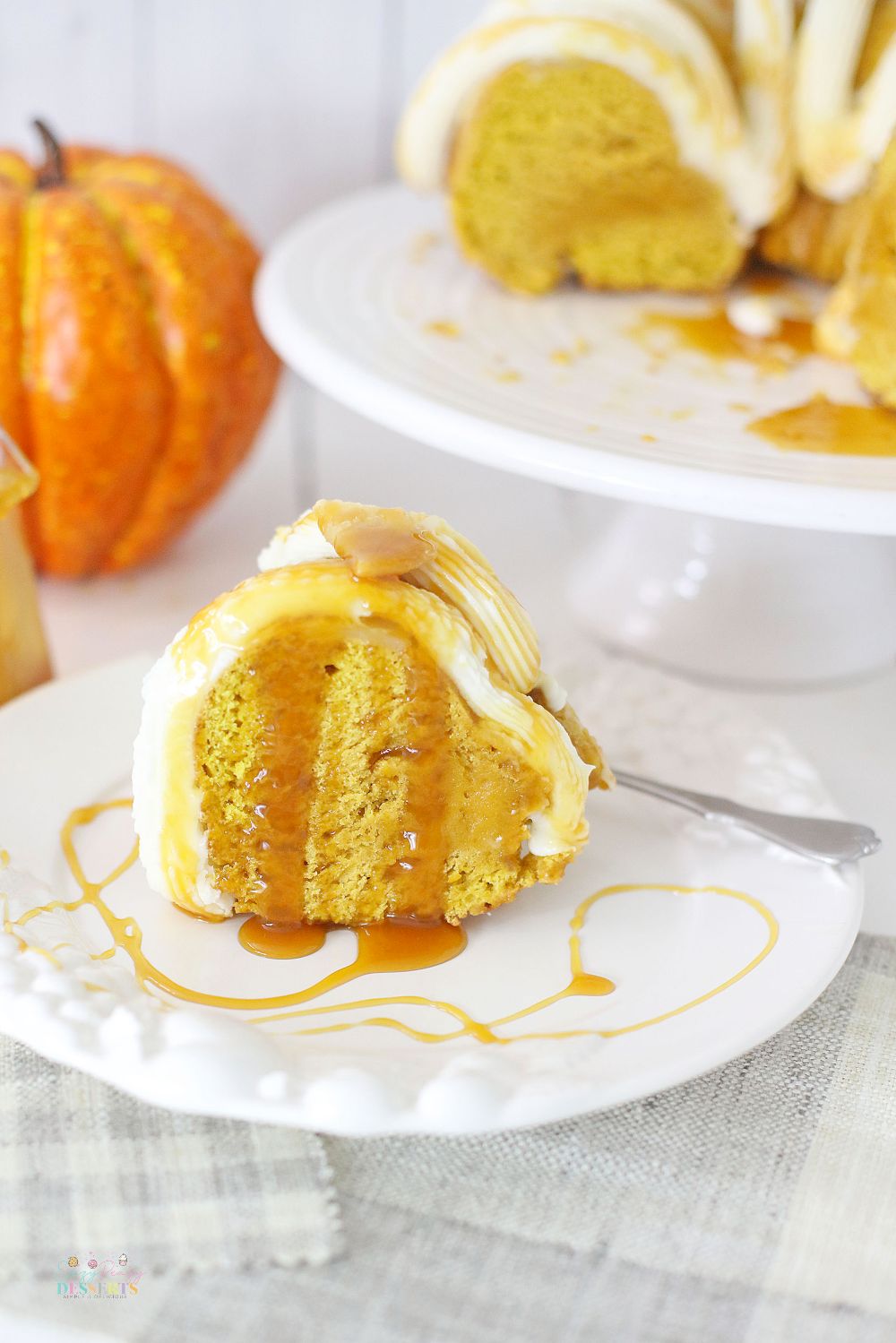 Close up image of a slice of pumpkin bundt cake with buttercream frosting, drizzled with caramel sauce