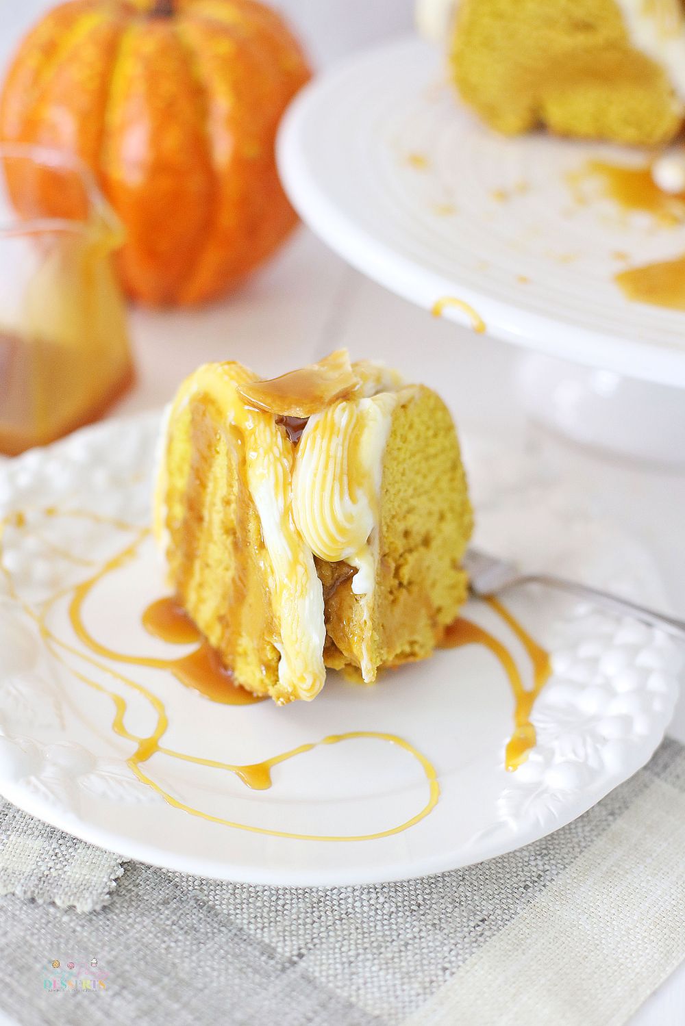 Image of a slice of pumpkin cake with fresh pumpkin, topped with buttercream frosting and drizzled with caramel sauce