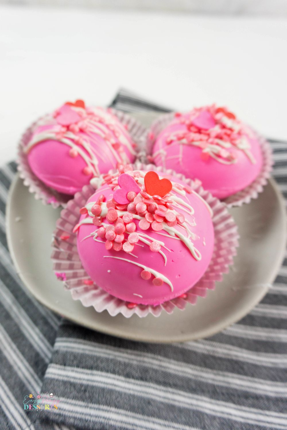 Image of three pink strawberry chocolate bombs on a dessert plate