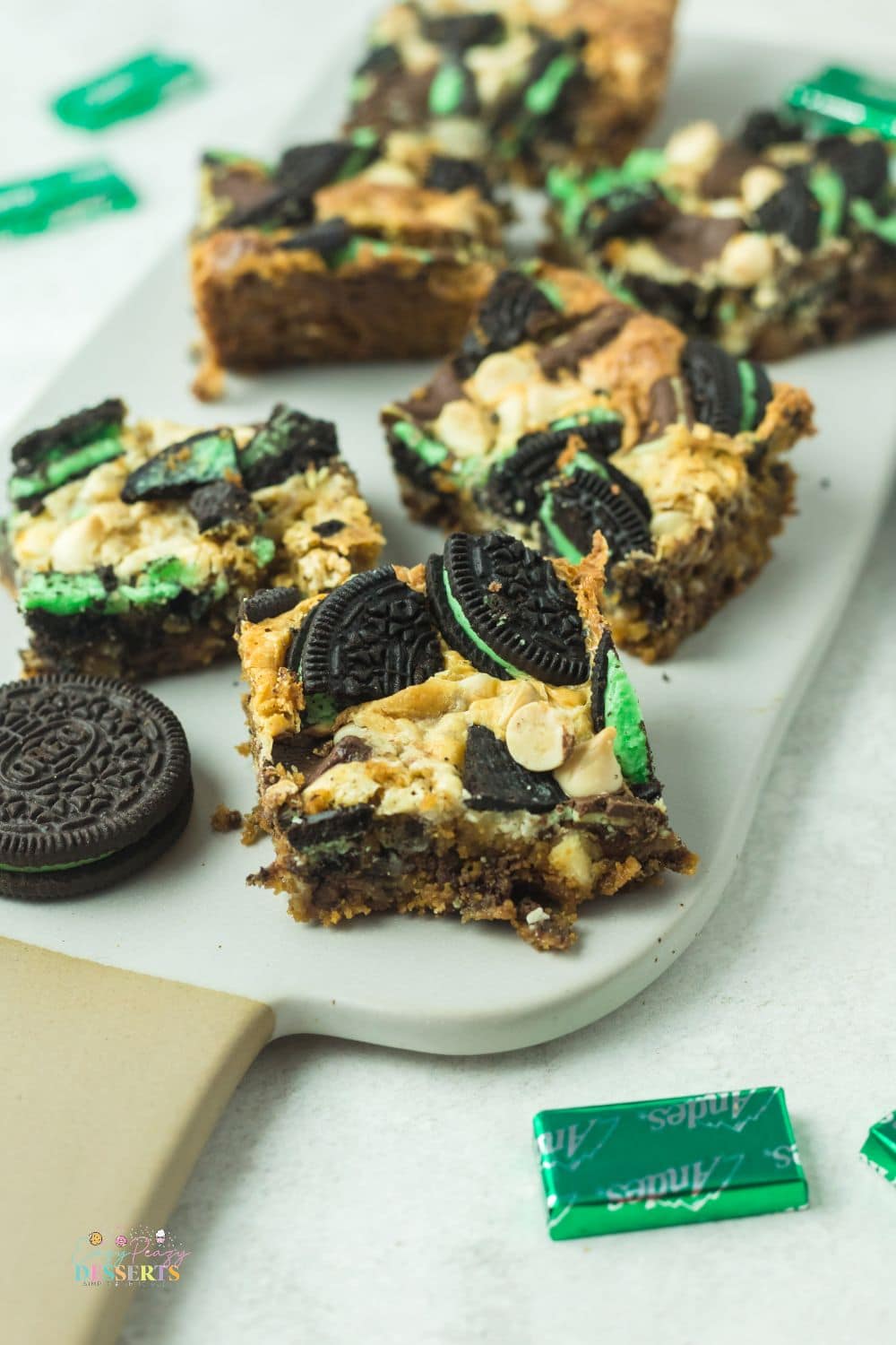 Image of mint cookie bars on a white serving plate with Andes mints and mint Oreo cookies on a side